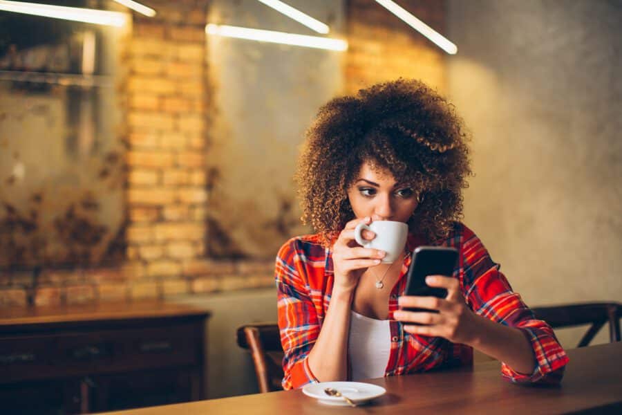 The girl is drinking coffee while looking at the phone